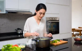 Seorang perempuan sedang memasak sayur memakai kompor induksi.
