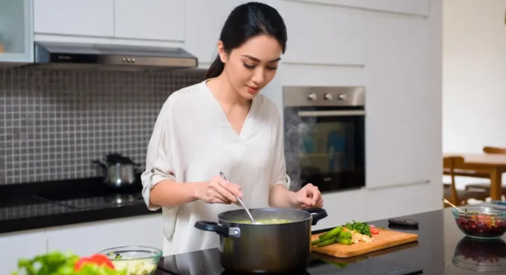 Seorang perempuan sedang memasak sayur memakai kompor induksi.