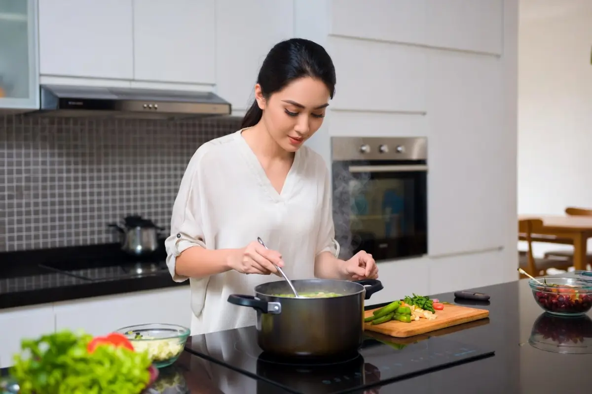 Seorang perempuan sedang memasak sayur memakai kompor induksi.