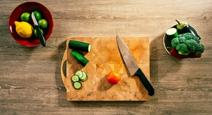 Talenan dengan pisau dan potongan sayuran di atasnya.