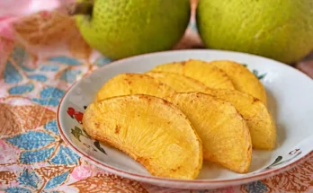 Sukun goreng disajikan di atas piring dengan latar belakang buah sukun yang masih utuh.