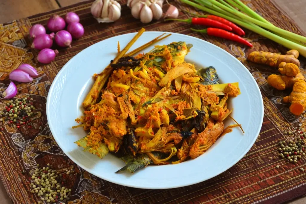 Arsik ikan disajikan di atas piring dan dikelilingi bumbu dapur antara lain bawang merah, bawang putih, cabai, serai, dan andaliman.